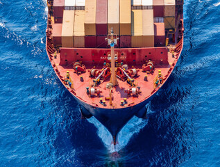 Aerial overhead close-up view of a bow of a container cargo ship traveling over blue ocean with...