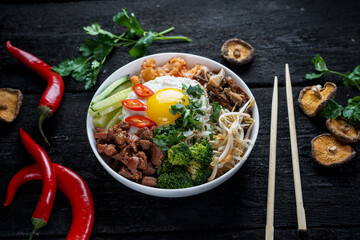 bibimbap with mushrooms, sprouts and meat on a plate on a dark background