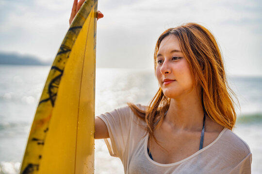 Surfer enjoys a sunny day at the beach while holding a yellow surfboard and smiling, with ocean waves in the background