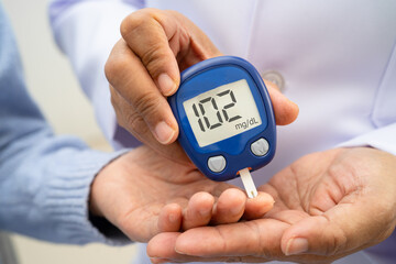 Asian doctor using digital glucose meter for check sample blood sugar level to treatment diabetes.
