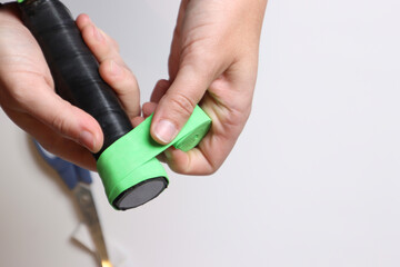 Woman wrapping a green over grip in a Pickleball paddle in a light background showing very close...