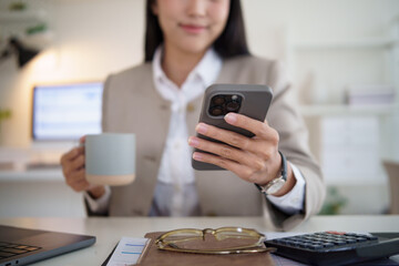Close up of businesswoman checking her smartphone while enjoying coffee at her desk.