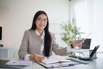 Smiling Asian businesswoman analyzing financial reports in a bright workspace.