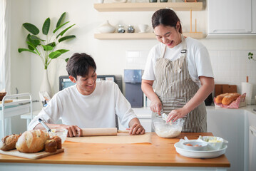Happy young couple preparing bread and desserts on a wooden table in a warm and bright kitchen.