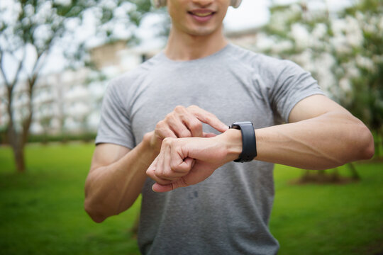 Close up of sporty male using smartwatch to track fitness progress post exercise in a park. Healthy lifestyle concept.