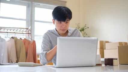 Young online seller working on laptop for online store management in a home office. E-commerce...