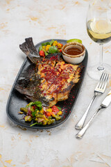 fried whole fish cut in half on a black plate with greens on a background with wine