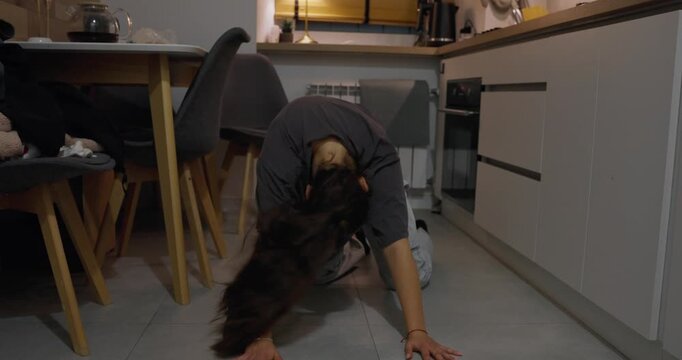 Girl in casual sits on the floor and dances slow dance in the style of self-reflection and modern dance at home in the kitchen in the evening