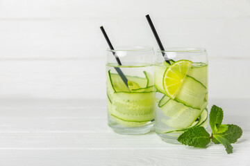 Cucumber water with lemon, lime and mint on a wooden table. Water infused with sliced ​​cucumber in a drinking glass. Tonic refreshing drink. Cucumber lemonade.Summer natural cooling drink.Copy space