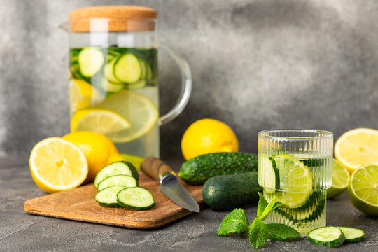 Cucumber water with lemon, lime and mint on a wooden table. Water infused with sliced ​​cucumber in a drinking glass. Tonic refreshing drink. Cucumber lemonade.Summer natural cooling drink.Copy space