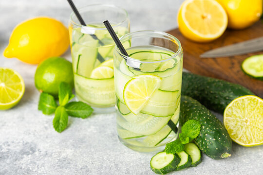 Cucumber water with lemon, lime and mint on a wooden table. Water infused with sliced ​​cucumber in a drinking glass. Tonic refreshing drink. Cucumber lemonade.Summer natural cooling drink.Copy space
