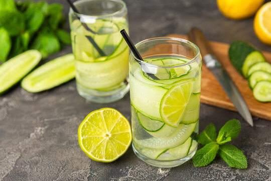 Cucumber water with lemon, lime and mint on a wooden table. Water infused with sliced ​​cucumber in a drinking glass. Tonic refreshing drink. Cucumber lemonade.Summer natural cooling drink.Copy space