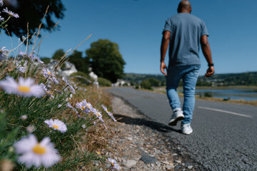 A man walks along a picturesque pathway lined with flowers, capturing a moment of leisure and exploration in a beautiful natural landscape under a bright blue sky.