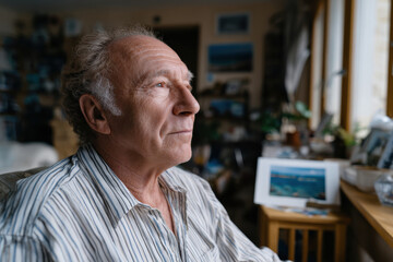 In this image, an elderly man stares thoughtfully, surrounded by a cluttered artistic space filled with pictures and personal memorabilia, reflecting a lifetime of experiences.
