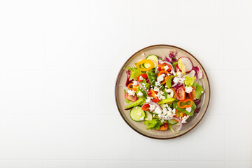 Cucumber salad on a wooden background.Homemade salad with fresh vegetables, cucumber, tomato, sweet pepper and lettuce in a plate.Vegetarian spring salad.Vegetarian diet.Healthy eating.Space for text