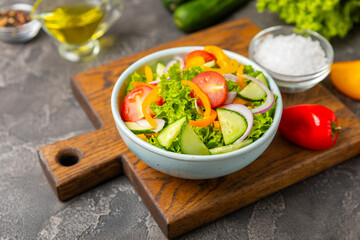 Cucumber salad on a wooden background.Homemade salad with fresh vegetables, cucumber, tomato, sweet pepper and lettuce in a plate.Vegetarian spring salad.Vegetarian diet.Healthy eating.Space for text
