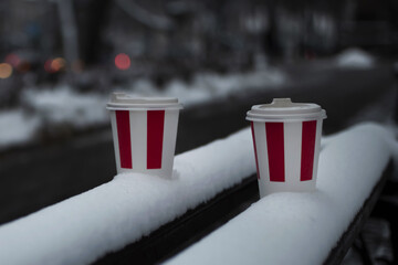 Cardboard coffee cups on a bench in winter. Lonely disposable coffee cups on a snow-covered bench in the evening