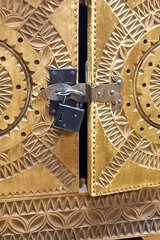 Locked wooden door features intricate carvings and padlock, symbolizing mystery and craftsmanship