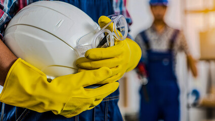Close-up of gloved hands holding a safety helmet and goggles, highlighting essential personal protective equipment for workplace safety.