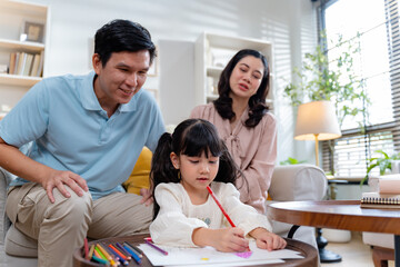 Obraz premium Asian Dad and Mom teaching daughter at home.Asian parents helping their daughter with homework at home.educational creative activity,imagination,study at home,family relationship,home school concept 