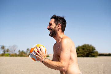 Happy man holding soccer ball on beach, enjoying summer vacation