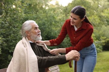 Smiling caregiver supporting elderly man with walking cane outdoors