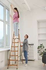Couple putting up curtains using ladder in room