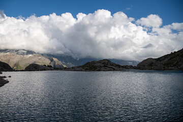 Tranquil view of Lac Blanc near Col des Montets in the French Alps, with dramatic clouds above alpine peaks. Serene mountain lake surrounded by rocky terrain and high-altitude beauty.