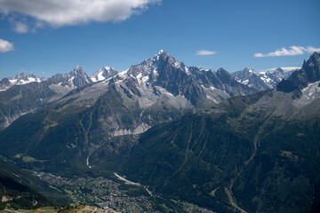 Stunning mountain range near Chamonix in the French Alps under clear blue sky. Jagged peaks, rocky ridges, and lush alpine slopes create a dramatic high-altitude landscape.