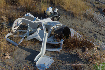 A pile of abandoned plastic chairs and other trash is seen on a sandy, overgrown landscape on a...
