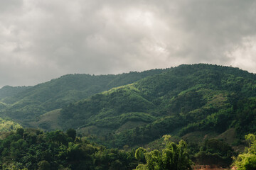 Rolling green hills and mountains under a cloudy, overcast sky. Lush vegetation covers the slopes.