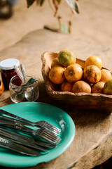 Rustic table setting with a wooden bowl of kumquats, silverware, and a teal plate. Warm, inviting, and natural.