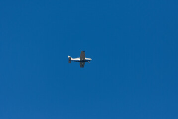 A small, blue and white propeller plane is flying high in a clear, blue sky on a bright day.