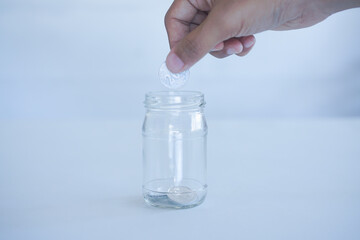 Hand putting coin into glass container,coins in a glass jar against ,savings coins - Investment And...