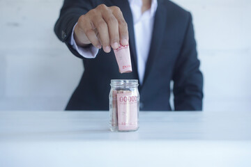 Male hand drops a bunch of  Indonesian Rupiah banknotes in glass jar on white background