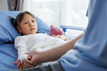 asian girl patient lying in hospital bed with bandaged hand and IV line, holding hands with nurse, doctor, medical professional or father. healthcare with compassion, trust and emotional support.