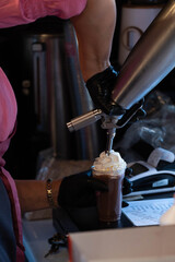 Owner of a small street food business filling with whipped cream a delicious chocolate milkshake.