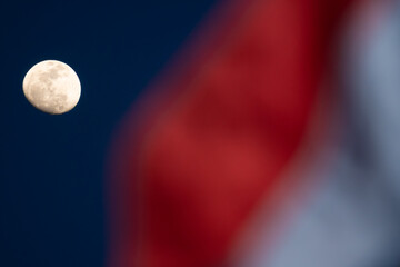 A photograph of a moon shining in the evening sky, with the waving flag of the Republic of Indonesia in the foreground, illustrates that the Republic of Indonesia is entering its independence month.