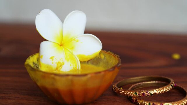 Closeup homemade ubtan facial in bowl with a big white champa flower. Ayurvedic face pack of Haldi (Turmeric), Rose water and gram flour. Natural beauty and skincare using since ancient India