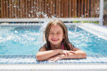 Cute smiling girl in a jacuzzi pool with blue refreshing water at an open-air resort. Bright sunny...
