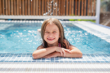 Cute smiling girl in a jacuzzi pool with blue refreshing water at an open-air resort. Bright sunny...