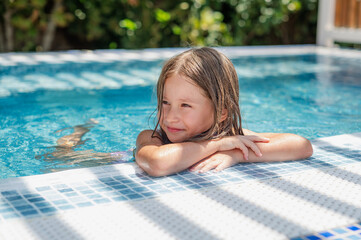 Cute smiling girl in a summer pool with blue refreshing water at an open-air resort. Bright sunny...