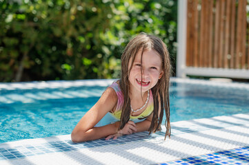 Cute smiling girl in a jacuzzi pool with blue refreshing water at an open-air resort. Bright sunny...