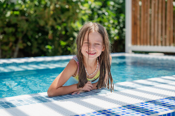 Cute smiling girl in a jacuzzi pool with blue refreshing water at an open-air resort. Bright sunny...