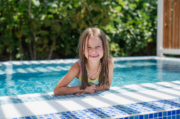 Cute smiling girl in a jacuzzi pool with blue refreshing water at an open-air resort. Bright sunny...