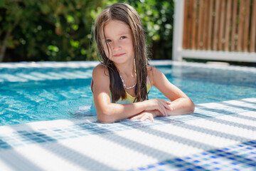 Cute smiling girl in a summer pool with blue refreshing water at an open-air resort. Bright sunny...