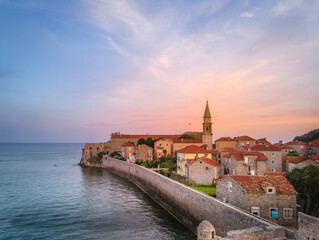 Picturesque sunset view of Budva Old Town in Montenegro with stone houses, red rooftops, a church...