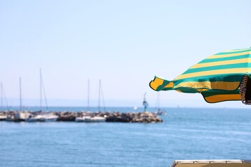 Bright green and yellow striped sun umbrella near the sea with sailboats and marina in the blurred...