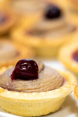 Close-up of a mini tart with creamy filling and glossy cherry topping, isolated on white background, showcasing vibrant colors and fine dessert details.