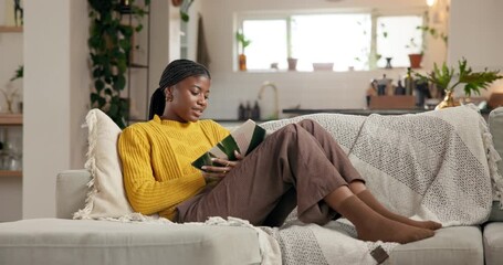 Reading, relax and weekend with black woman on sofa in living room of home for literature hobby. Book, break and storytelling with person chilling in apartment for me time, novel or wellness